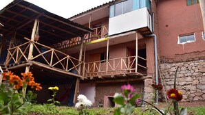 Un edificio con una struttura di balcone in legno, un muro in pietra e vegetazione sullo sfondo.