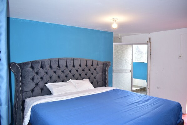 A bedroom with a large bed, a tufted headboard, and a blue wall. - Chillhouse pisac (Pisac)