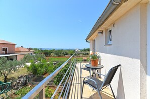 Un balcón con mesa y sillas, con vista a un jardín y al mar.
