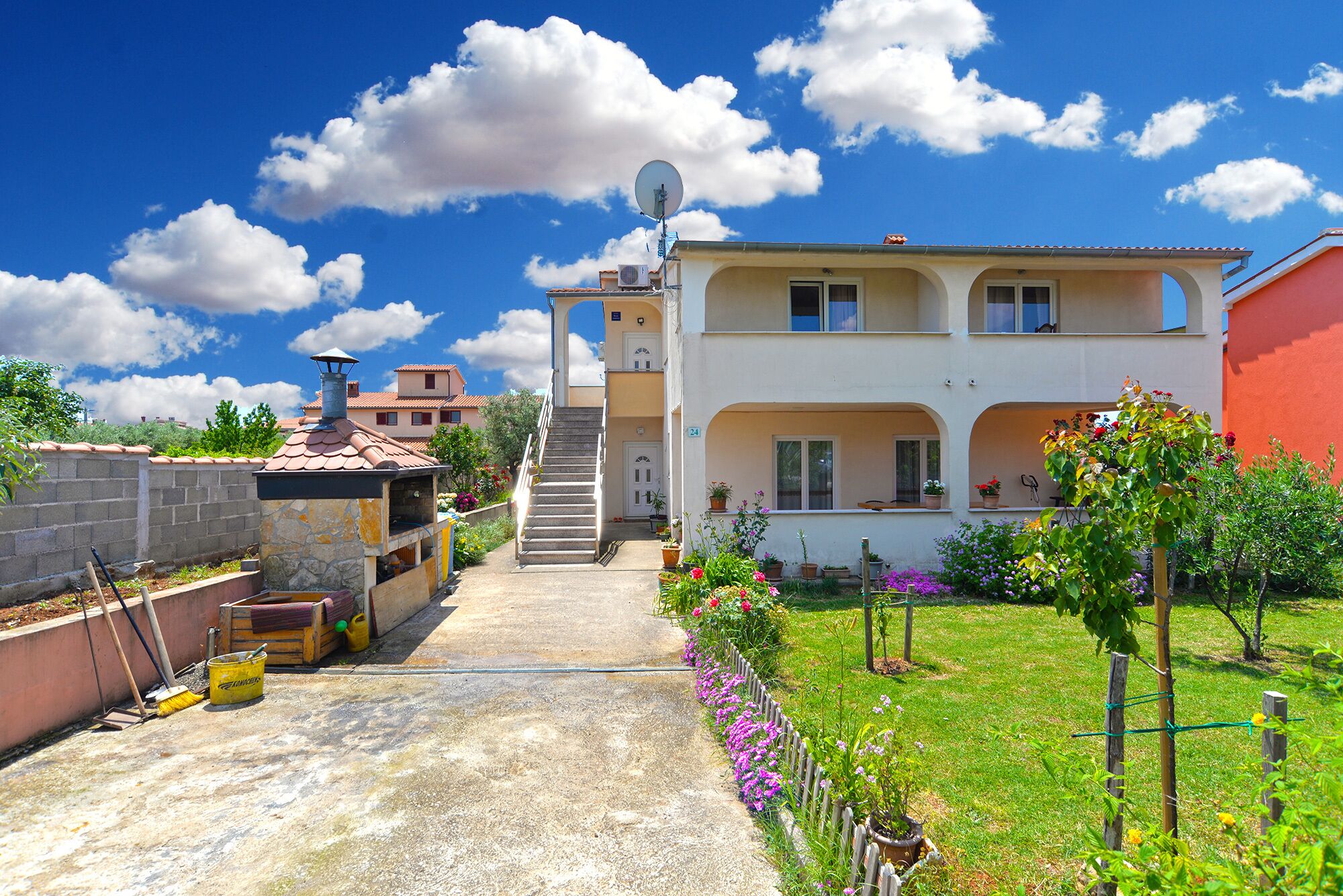 A two-story house with a garden, a satellite dish, and a staircase leading to the upper floor.