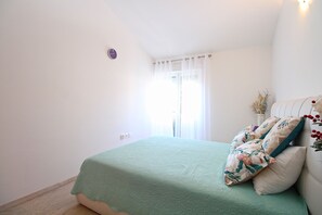 A bedroom with a bed, a nightstand, a window with curtains, and a wall clock.