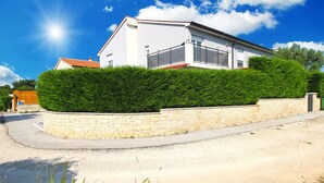 Una casa moderna de dues plantes amb un mur de contenció de pedra i una tanca metàl·lica.