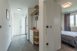 A modern hotel room with a walk-in closet, a bed with patterned bedding, and a window with curtains.