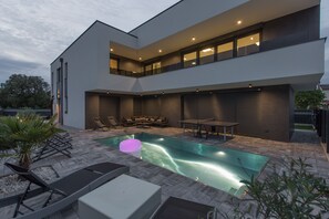 A modern two-story house with a swimming pool, outdoor seating, and a patio area.