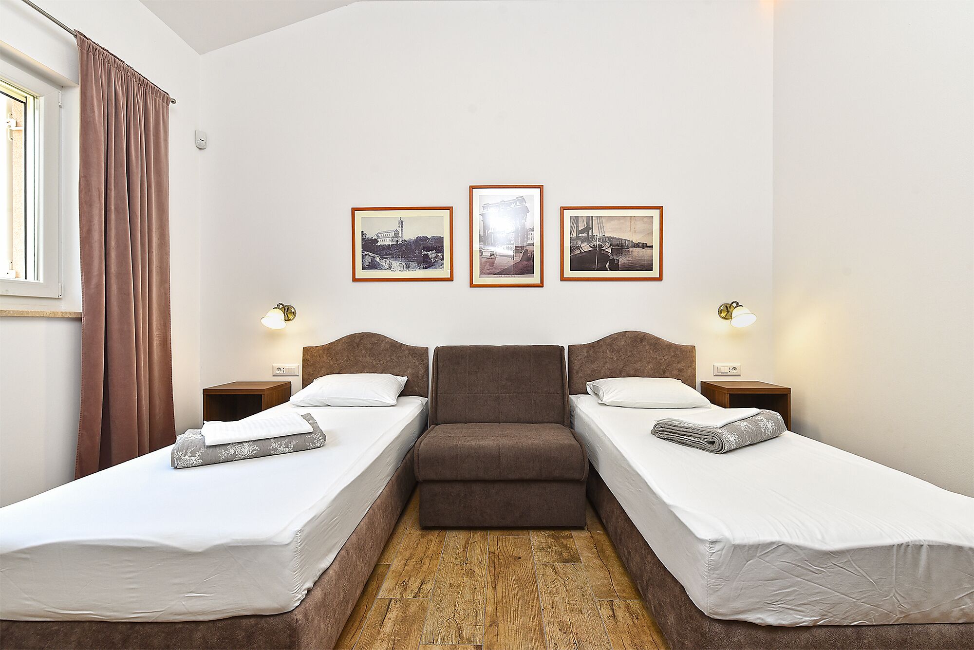 A hotel room with two single beds, a sofa bed, and three framed pictures on the wall.