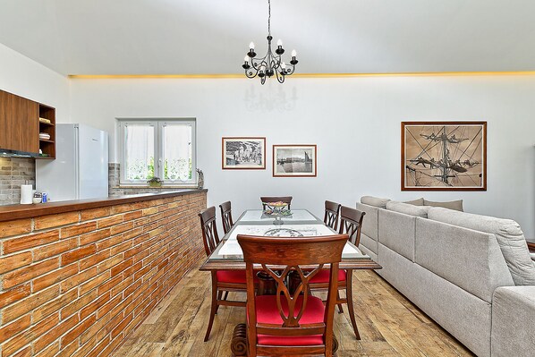 A modern kitchen with a brick backsplash, a dining table with chairs, a sofa, and a chandelier.