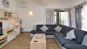 A modern living room with a grey sectional sofa, a wooden coffee table, a TV on a wooden stand, and a wall-mounted clock. - Villa 2273/75669 (Istria - Liznjan), 800m from the beach (Liznjan)