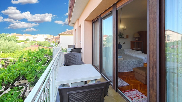 A balcony with a table and chairs, a bed with a wooden headboard, and a sliding glass door leading to a room. - Apartment 2276/75855 (Istria - Pula), 3500m from the beach (Pula)