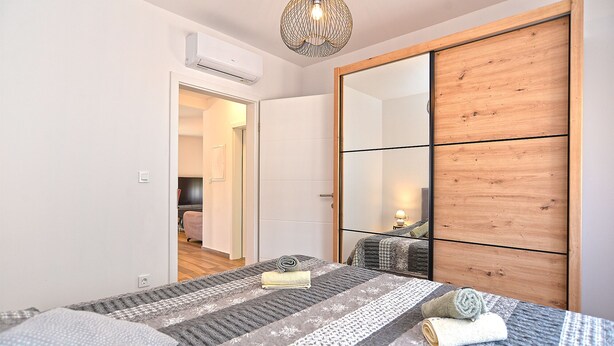 A bedroom with a bed, a wooden wardrobe, a mirror, and a hanging light fixture. - House 2279/75934 (Istria - Medulin), 350m from the beach (Medulin)