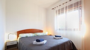 A neatly made bed with a grey bedspread, two folded towels, and a bedside lamp on a wooden nightstand. - Apartment 2281/76013 (Istria - Pula), 2500m from the beach (Pula)