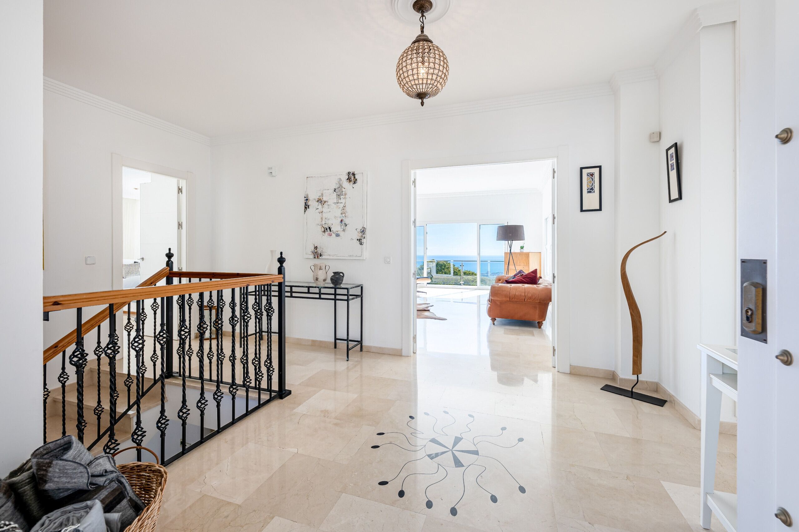 A spacious hallway with a wooden staircase, a decorative floor pattern, and a view to a balcony.