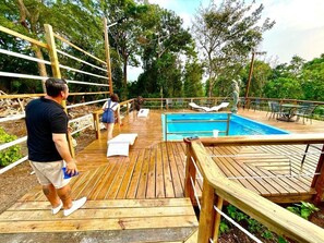 A wooden deck with a pool, lounge chairs, and a statue.