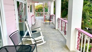 Een overdekt terras met stoelen en een tafel, omgeven door witte hekwerken en roze details.