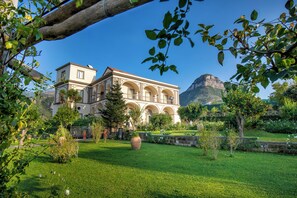 A large, historic building with multiple arches and a prominent mountain in the background.