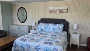 Een slaapkamer met een bed, nachtkastje, dressoir, bank en een rode poef.