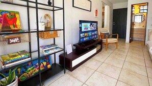 Ein Wohnzimmer mit Fernseher, Regalen mit Büchern und Dekoration, einem Sessel und einer Tür.