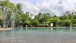 Une piscine avec une fontaine, entourée d’arbres et d’une clôture.