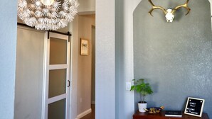 Un couloir agrémenté d’un luminaire décoratif au plafond, d’un crâne monté sur le mur avec des bois de cerf, d’une pancarte d’accueil encadrée et d’une plante en pot.