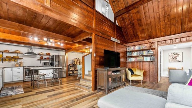 A spacious living area with a wooden ceiling, a kitchen with modern appliances, and a comfortable seating area with a sofa and armchairs. - Book-Me-By-The-Lake (Morgantown)