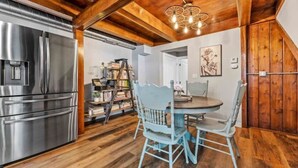 A kitchen with a stainless steel refrigerator, wooden ceiling beams, and a dining area with a round table and two chairs. - Book-Me-By-The-Lake (Morgantown)