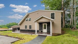 A two-story house with a stone foundation, a front porch, and a driveway leading to the entrance. - Book-Me-By-The-Lake (Morgantown)