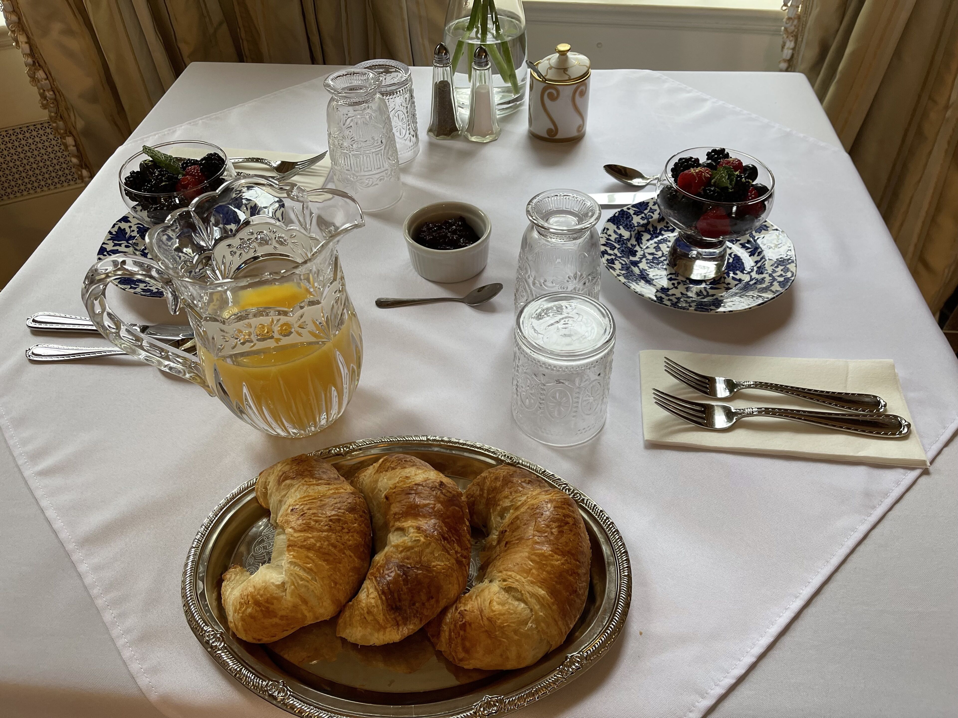 Une table de petit-déjeuner avec des croissants, un pichet de jus d’orange et divers condiments.