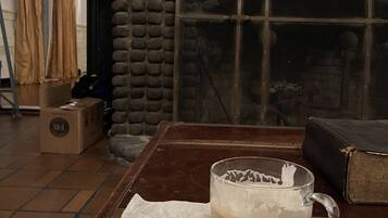 A rustic room with a stone wall, a wooden table with a mug and a bagel, and a bookshelf with books and a globe.