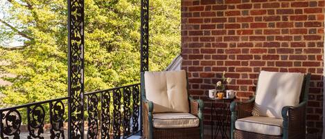 A balcony with wicker chairs and a small table with a vase and two cups.