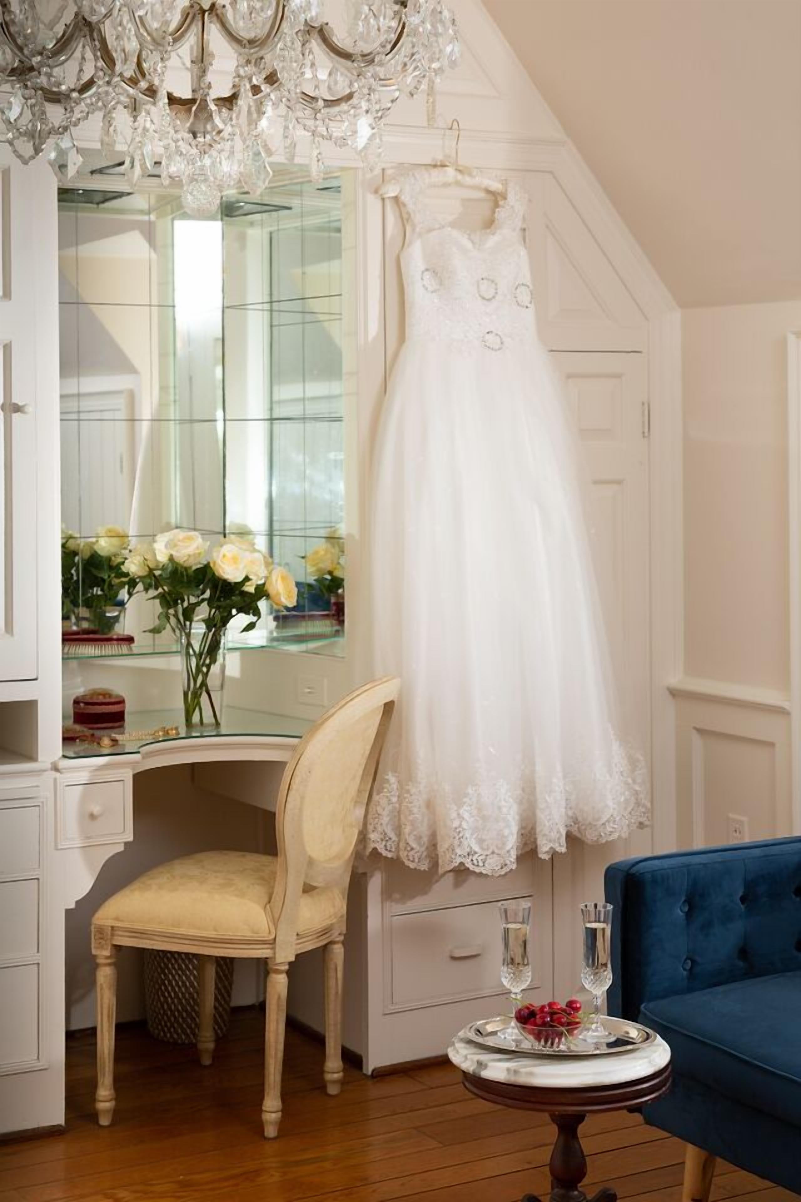 A room with a white dress hanging on a wall, a chair, a blue sofa, a small table with a tray of fruit and glasses, and a chandelier.