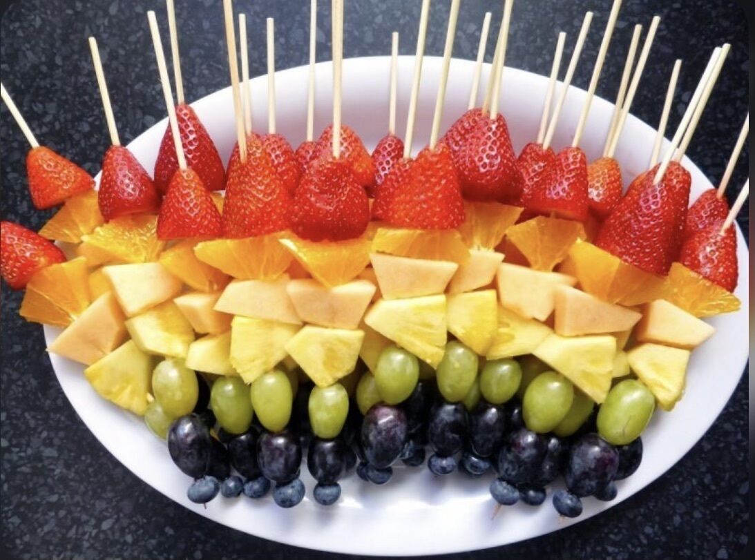 En tallerken med frugtspyd fyldt med jordbær, melon, ananas, druer og blåbær.