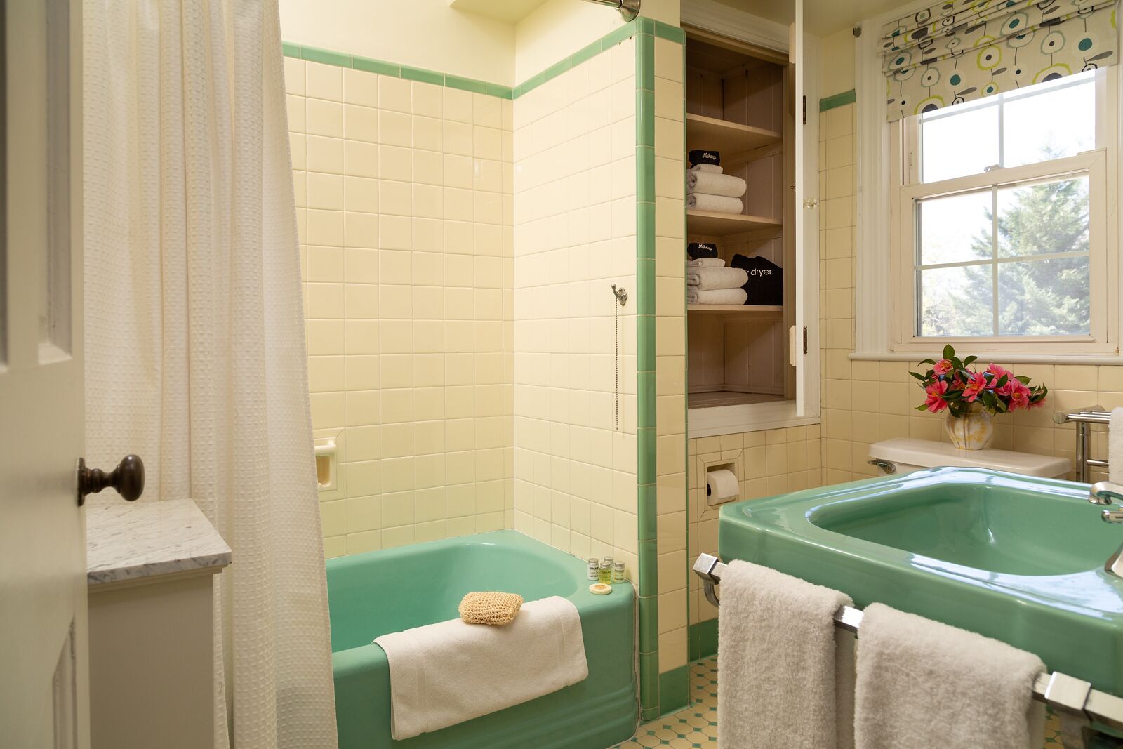 Un baño con una bañera verde, un lavabo y una ventana con flores.
