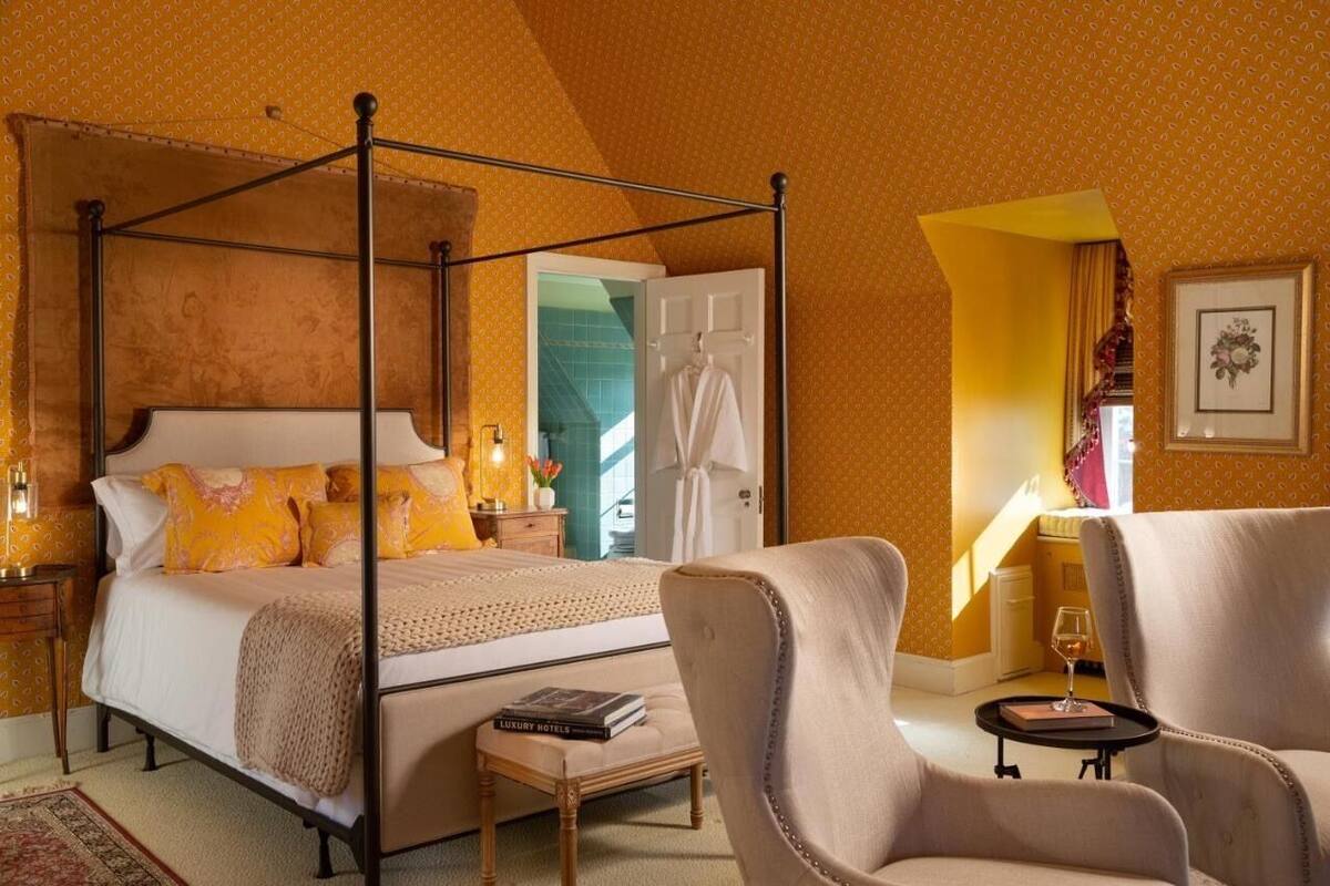 Un lit à baldaquin avec une tête de lit blanche, une table de chevet avec une lampe et une chaise avec une petite table à côté.