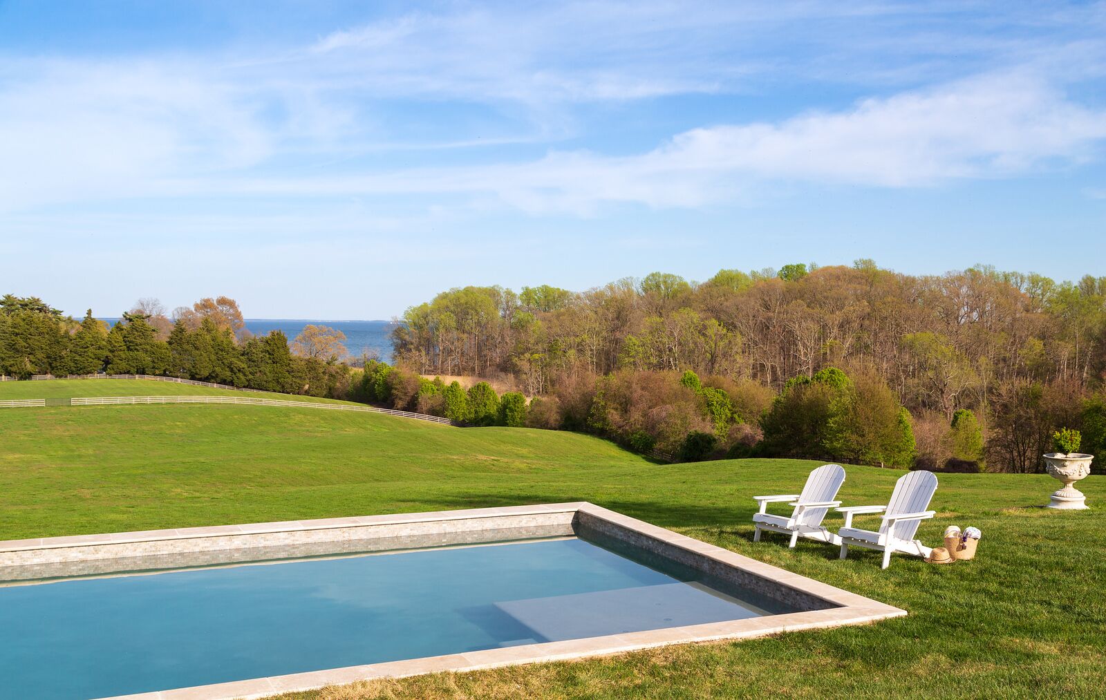 Una piscina con due poltrone Adirondack e un vaso decorativo sull'erba.