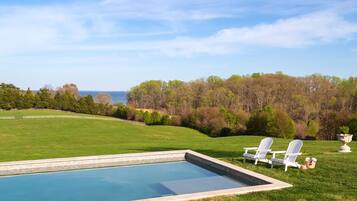 A swimming pool with two Adirondack chairs and a decorative urn on the grass.