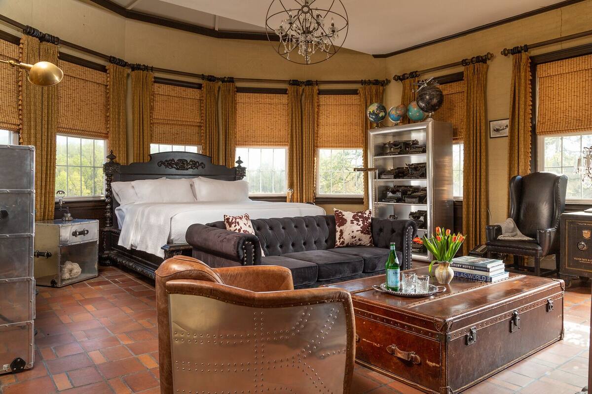 Une chambre spacieuse avec un grand lit, un fauteuil en cuir, une commode en bois et une collection de globes terrestres accrochés au mur.