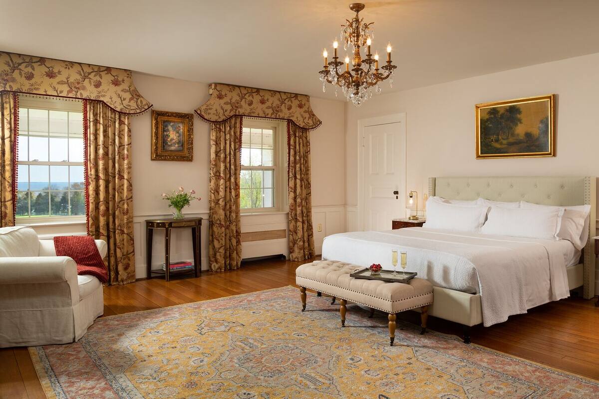Une chambre spacieuse avec un grand lit, un lustre, un tableau et une vue sur l’extérieur.