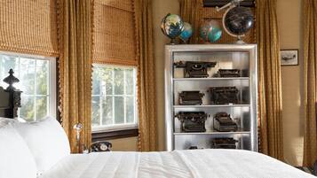 A bedroom with a large bed, a vintage globe collection, and a shelf of old typewriters.