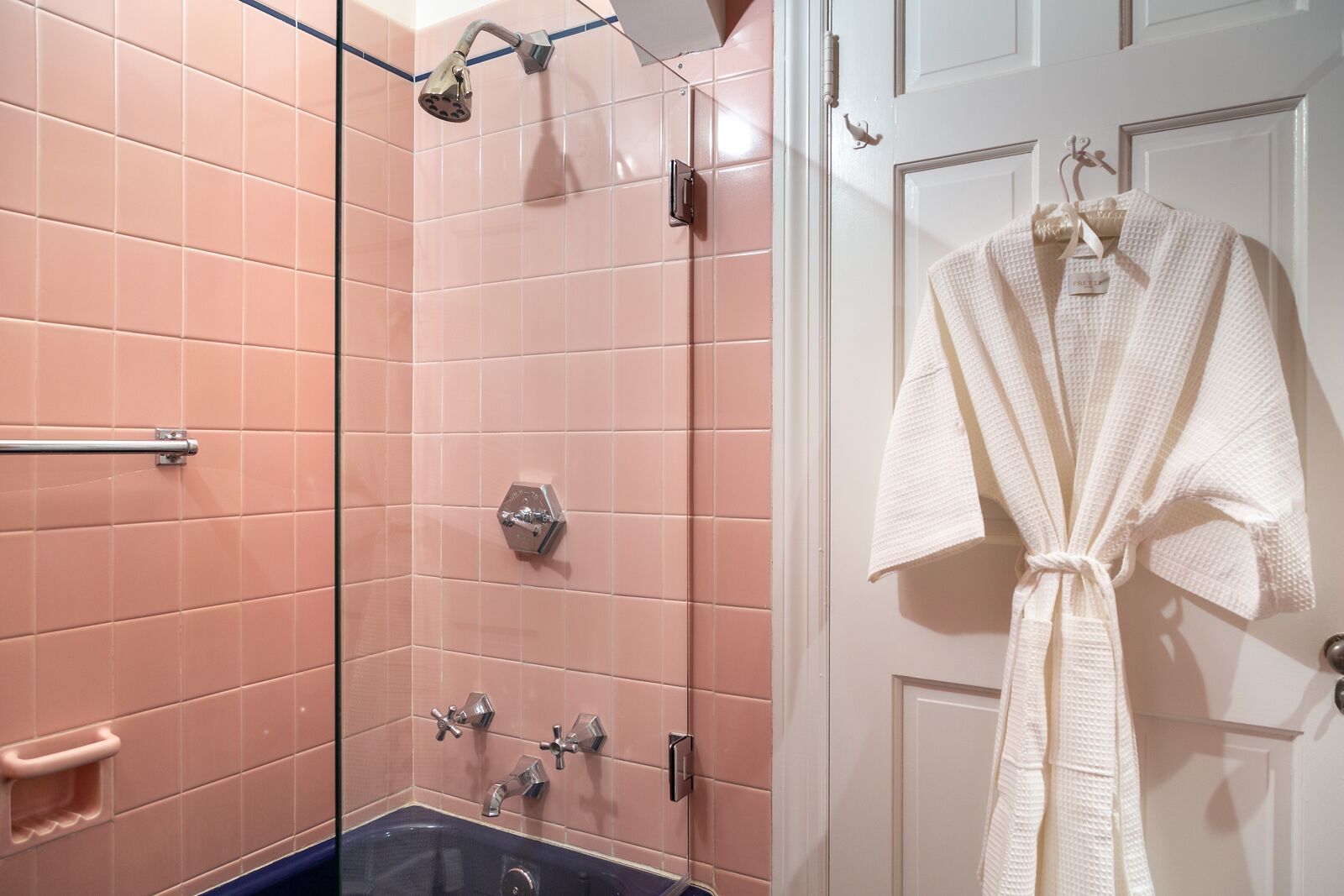 Ein Badezimmer mit rosa Fliesen, einer Badewanne, einer Dusche und einem Bademantel, der an der Tür hängt.