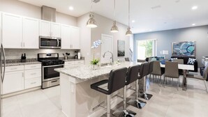 A modern kitchen with white cabinets, stainless steel appliances, and a central island with bar stools. - 4 Suites Villa 5 min to Disney (Kissimmee)