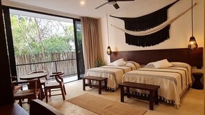 Een slaapkamer met twee bedden, een plafondventilator, een hangmat, een eethoek met een tafel en stoelen, en uitzicht op groen buiten.