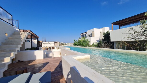 Een modern resort met een zwembad, houten terras en witte gebouwen.