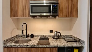 Een kleine keuken met een inbouwmagnetron, een spoelbak, een waterkoker en een vaatwasser.