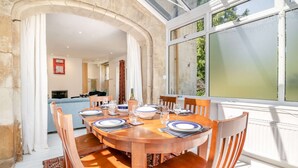 Uma sala de jantar com uma mesa redonda de madeira posta para quatro pessoas, rodeada por cadeiras de madeira.