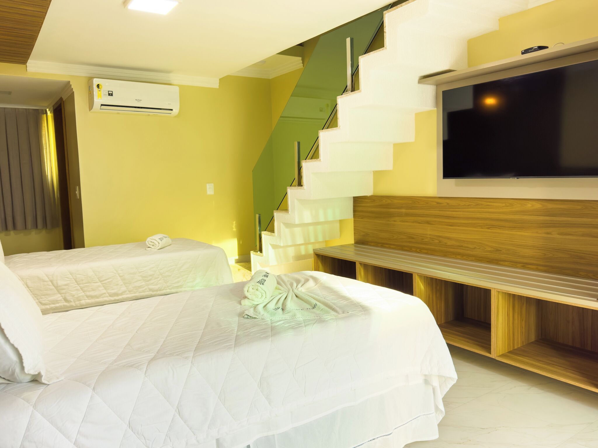 Una habitación de hotel con cama, televisión, escalera y equipo de aire acondicionado.
