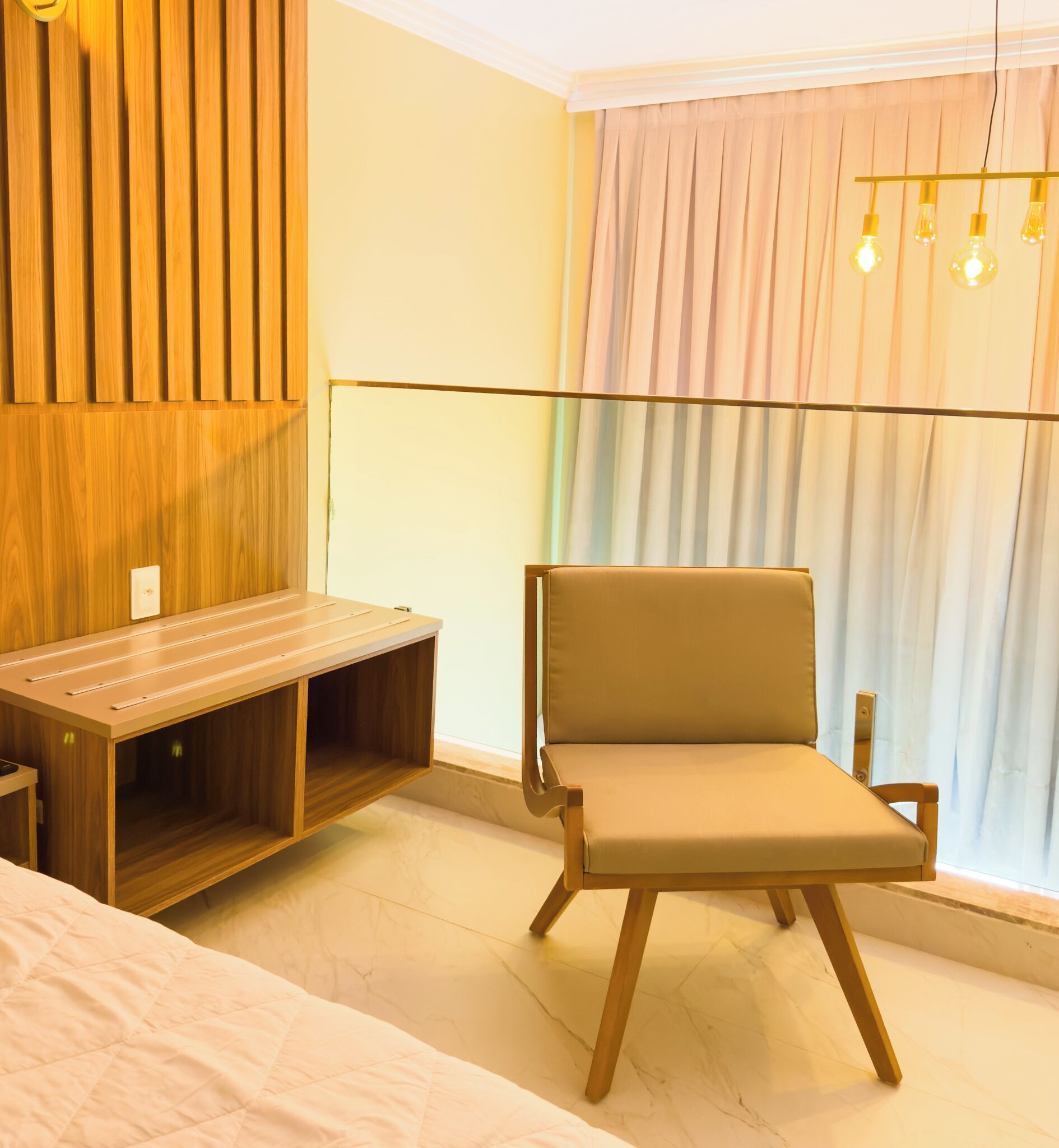 Una habitación moderna con un escritorio de madera, una silla acolchada, una cama y un gran ventanal con cortinas.