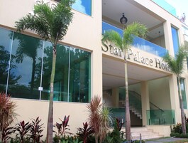 Entrada de un hotel con un letrero que dice 'Star Palace Hotel', una escalera de cristal y palmeras a su alrededor.