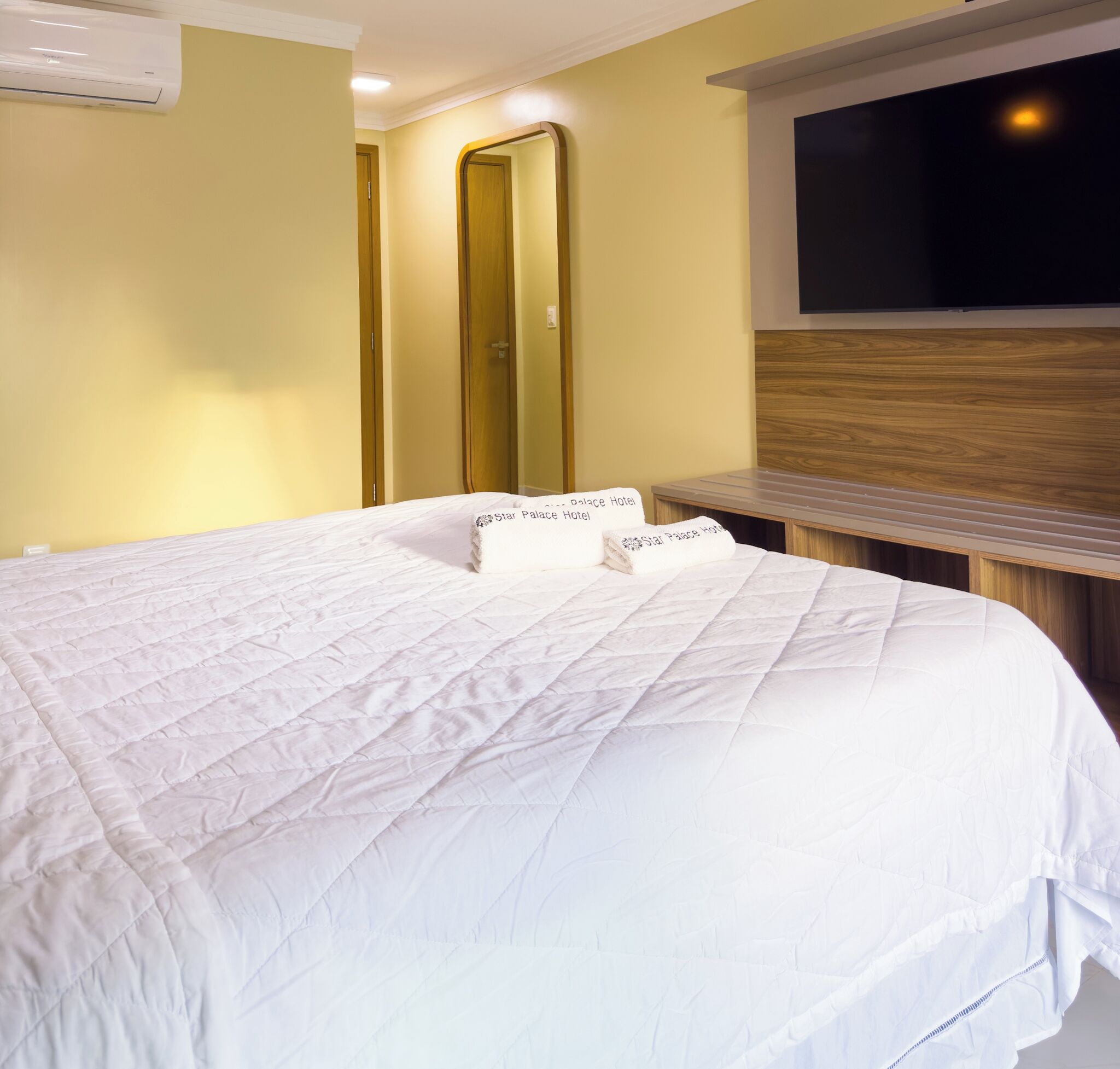 A hotel room with a large bed, a wooden headboard, a mirror, and a window.