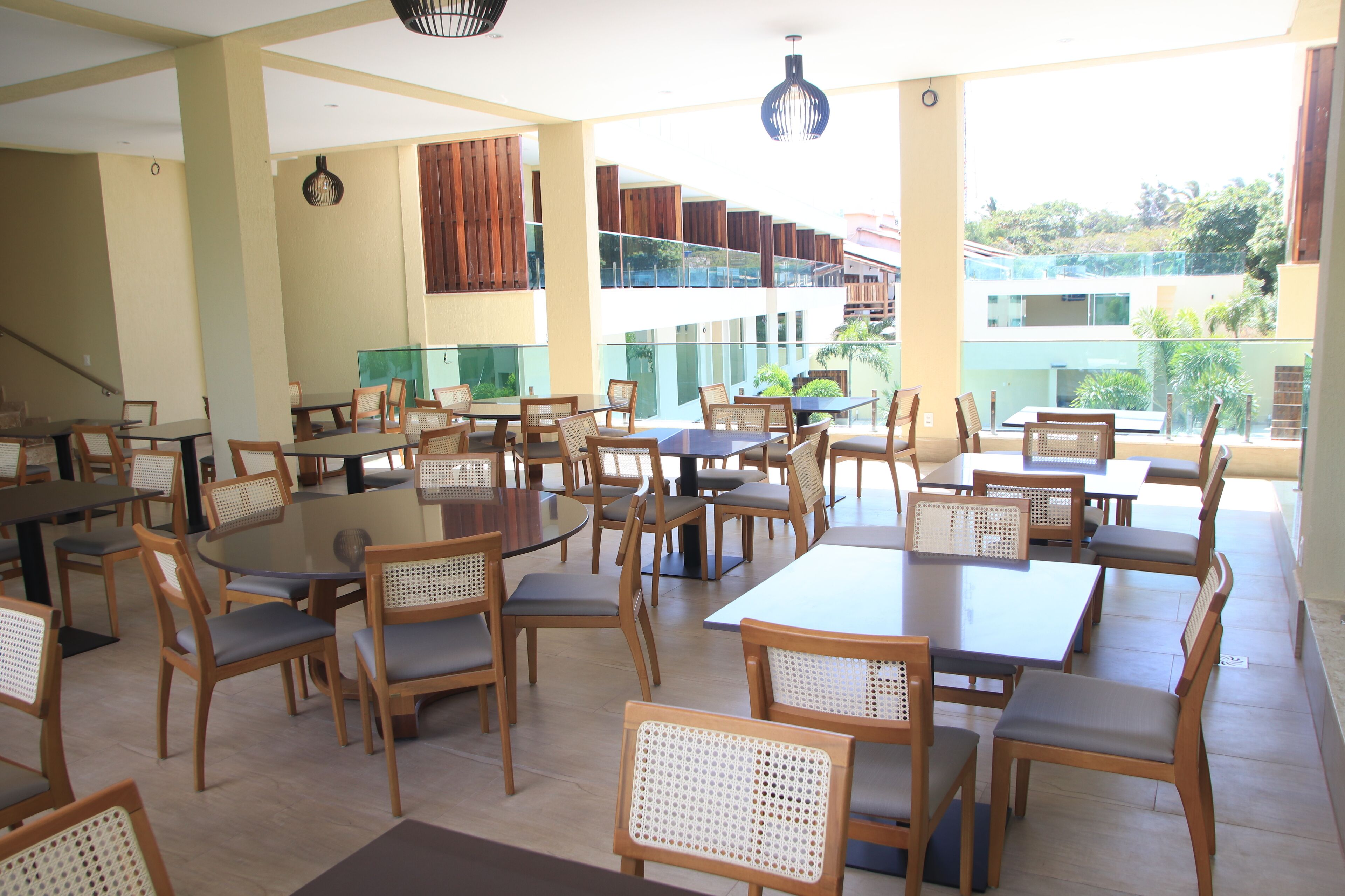 A spacious indoor dining area with multiple tables and chairs, large windows offering a view of the surrounding buildings and greenery.