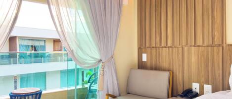A modern hotel room with a balcony, a wooden wall panel, a bed, a chair, and a small table.