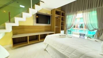 A modern hotel room with a large bed, a flat-screen TV mounted on the wall, a wooden bench, and a view of a swimming pool.